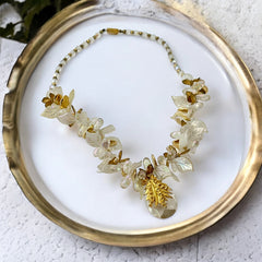 Vintage French necklace from the 1980s featuring iridescent acrylic beads, frosted and clear leaf accents, gold-tone metal details, and a central faceted pear-shaped drop with floral embellishment. Nature-inspired design in very good vintage condition