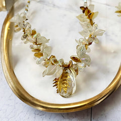 Vintage French necklace from the 1980s featuring iridescent acrylic beads, frosted and clear leaf accents, gold-tone metal details, and a central faceted pear-shaped drop with floral embellishment. Nature-inspired design in very good vintage condition