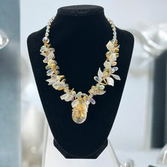 Vintage French necklace from the 1980s featuring iridescent acrylic beads, frosted and clear leaf accents, gold-tone metal details, and a central faceted pear-shaped drop with floral embellishment. Nature-inspired design in very good vintage condition