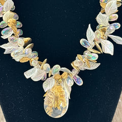 Vintage French necklace from the 1980s featuring iridescent acrylic beads, frosted and clear leaf accents, gold-tone metal details, and a central faceted pear-shaped drop with floral embellishment. Nature-inspired design in very good vintage condition