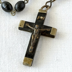 Vintage French ebony and silver‑tone rosary with black boxwood beads and signed cross, photographed on light fabric background.