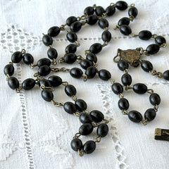 Vintage French ebony and silver‑tone rosary with black boxwood beads and signed cross, photographed on light fabric background.