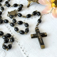 Vintage French ebony and silver‑tone rosary with black boxwood beads and signed cross, photographed on light fabric background.