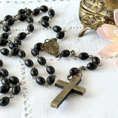 Vintage French ebony and silver‑tone rosary with black boxwood beads and signed cross, photographed on light fabric background.