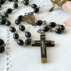 Vintage French ebony and silver‑tone rosary with black boxwood beads and signed cross, photographed on light fabric background.