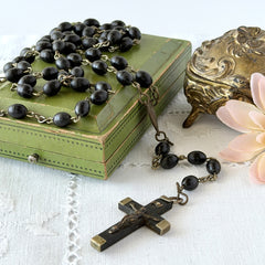Vintage French ebony and silver‑tone rosary with black boxwood beads and signed cross, photographed on light fabric background.