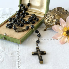Vintage French ebony and silver‑tone rosary with black boxwood beads and signed cross, photographed on light fabric background.