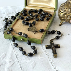 Vintage French ebony and silver‑tone rosary with black boxwood beads and signed cross, photographed on light fabric background.