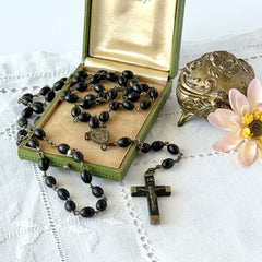Vintage French ebony and silver‑tone rosary with black boxwood beads and signed cross, photographed on light fabric background.