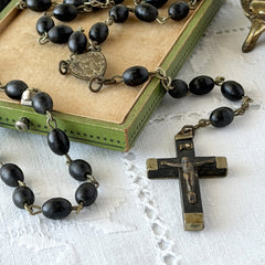 Vintage French ebony and silver‑tone rosary with black boxwood beads and signed cross, photographed on light fabric background.
