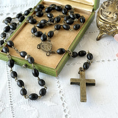 Vintage French ebony and silver‑tone rosary with black boxwood beads and signed cross, photographed on light fabric background.
