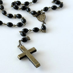 Vintage French ebony and silver‑tone rosary with black boxwood beads and signed cross, photographed on light fabric background.
