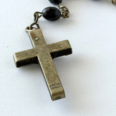 Vintage French ebony and silver‑tone rosary with black boxwood beads and signed cross, photographed on light fabric background.