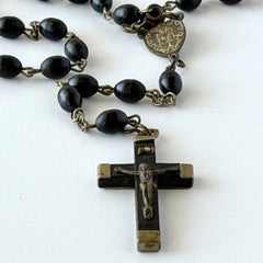 Vintage French ebony and silver‑tone rosary with black boxwood beads and signed cross, photographed on light fabric background.