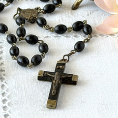 Vintage French ebony and silver‑tone rosary with black boxwood beads and signed cross, photographed on light fabric background.