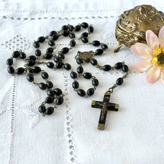 Vintage French ebony and silver‑tone rosary with black boxwood beads and signed cross, photographed on light fabric background.