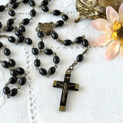 Vintage French ebony and silver‑tone rosary with black boxwood beads and signed cross, photographed on light fabric background.