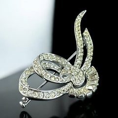 Vintage French bow brooch with clear rhinestones in rhodium-plated metal, featuring pavé chatons and baguettes in a sculptural 1950s design.