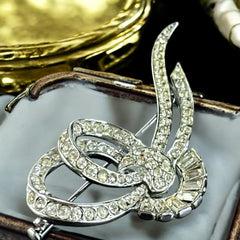 Vintage French bow brooch with clear rhinestones in rhodium-plated metal, featuring pavé chatons and baguettes in a sculptural 1950s design.