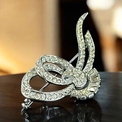 Vintage French bow brooch with clear rhinestones in rhodium-plated metal, featuring pavé chatons and baguettes in a sculptural 1950s design.