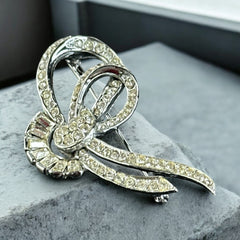 Vintage French bow brooch with clear rhinestones in rhodium-plated metal, featuring pavé chatons and baguettes in a sculptural 1950s design.
