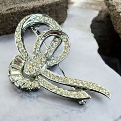 Vintage French bow brooch with clear rhinestones in rhodium-plated metal, featuring pavé chatons and baguettes in a sculptural 1950s design.