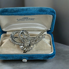 Vintage French bow brooch with clear rhinestones in rhodium-plated metal, featuring pavé chatons and baguettes in a sculptural 1950s design.