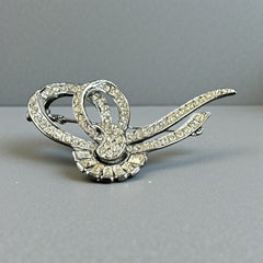 Vintage French bow brooch with clear rhinestones in rhodium-plated metal, featuring pavé chatons and baguettes in a sculptural 1950s design.