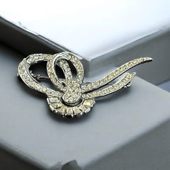 Vintage French bow brooch with clear rhinestones in rhodium-plated metal, featuring pavé chatons and baguettes in a sculptural 1950s design.