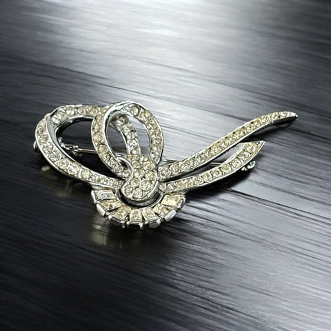 Vintage French bow brooch with clear rhinestones in rhodium-plated metal, featuring pavé chatons and baguettes in a sculptural 1950s design.