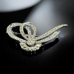 Vintage French bow brooch with clear rhinestones in rhodium-plated metal, featuring pavé chatons and baguettes in a sculptural 1950s design.