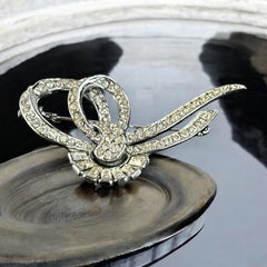 Vintage French bow brooch with clear rhinestones in rhodium-plated metal, featuring pavé chatons and baguettes in a sculptural 1950s design.
