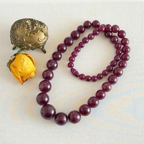 Vintage French plum‑colored graduated bead necklace with a matching screw clasp, shown on display props from multiple angles.
