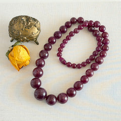 Vintage French plum‑colored graduated bead necklace with a matching screw clasp, shown on display props from multiple angles.