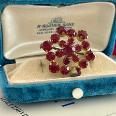 Vintage European brooch with red rhinestones set in gold tone metal, featuring a trombone clasp and floral starburst design, shown from multiple angles to highlight its mid-century craftsmanship and condition.