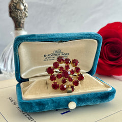 Vintage European brooch with red rhinestones set in gold tone metal, featuring a trombone clasp and floral starburst design, shown from multiple angles to highlight its mid-century craftsmanship and condition.