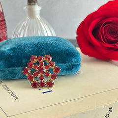 Vintage European brooch with red rhinestones set in gold tone metal, featuring a trombone clasp and floral starburst design, shown from multiple angles to highlight its mid-century craftsmanship and condition.