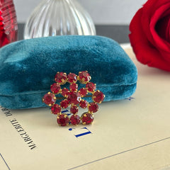 Vintage European brooch with red rhinestones set in gold tone metal, featuring a trombone clasp and floral starburst design, shown from multiple angles to highlight its mid-century craftsmanship and condition.