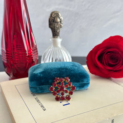 Vintage European brooch with red rhinestones set in gold tone metal, featuring a trombone clasp and floral starburst design, shown from multiple angles to highlight its mid-century craftsmanship and condition.