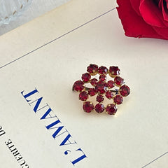 Vintage European brooch with red rhinestones set in gold tone metal, featuring a trombone clasp and floral starburst design, shown from multiple angles to highlight its mid-century craftsmanship and condition.