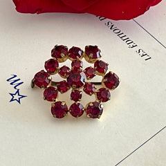 Vintage European brooch with red rhinestones set in gold tone metal, featuring a trombone clasp and floral starburst design, shown from multiple angles to highlight its mid-century craftsmanship and condition.