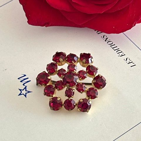 Vintage European brooch with red rhinestones set in gold tone metal, featuring a trombone clasp and floral starburst design, shown from multiple angles to highlight its mid-century craftsmanship and condition.