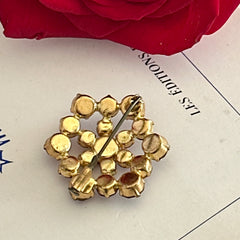 Vintage European brooch with red rhinestones set in gold tone metal, featuring a trombone clasp and floral starburst design, shown from multiple angles to highlight its mid-century craftsmanship and condition.