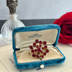 Vintage European brooch with red rhinestones set in gold tone metal, featuring a trombone clasp and floral starburst design, shown from multiple angles to highlight its mid-century craftsmanship and condition.