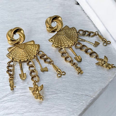 Vintage 1980s French stamped brass dangle earrings featuring a scallop shell centerpiece with eclectic dangling charms, including an owl, shovel, putti angel, axe, and scissors. Unique statement jewelry with a bold boho style, rich patina, and artistic character.