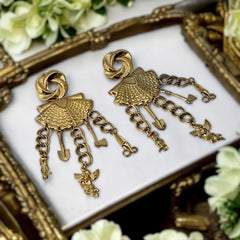 Vintage 1980s French stamped brass dangle earrings featuring a scallop shell centerpiece with eclectic dangling charms, including an owl, shovel, putti angel, axe, and scissors. Unique statement jewelry with a bold boho style, rich patina, and artistic character.