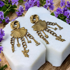Vintage 1980s French stamped brass dangle earrings featuring a scallop shell centerpiece with eclectic dangling charms, including an owl, shovel, putti angel, axe, and scissors. Unique statement jewelry with a bold boho style, rich patina, and artistic character.