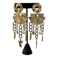 Vintage 1980s French stamped brass dangle earrings featuring a scallop shell centerpiece with eclectic dangling charms, including an owl, shovel, putti angel, axe, and scissors. Unique statement jewelry with a bold boho style, rich patina, and artistic character.