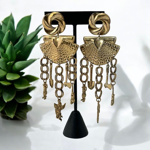 Vintage 1980s French stamped brass dangle earrings featuring a scallop shell centerpiece with eclectic dangling charms, including an owl, shovel, putti angel, axe, and scissors. Unique statement jewelry with a bold boho style, rich patina, and artistic character.