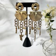 Vintage 1980s French stamped brass dangle earrings featuring a scallop shell centerpiece with eclectic dangling charms, including an owl, shovel, putti angel, axe, and scissors. Unique statement jewelry with a bold boho style, rich patina, and artistic character.